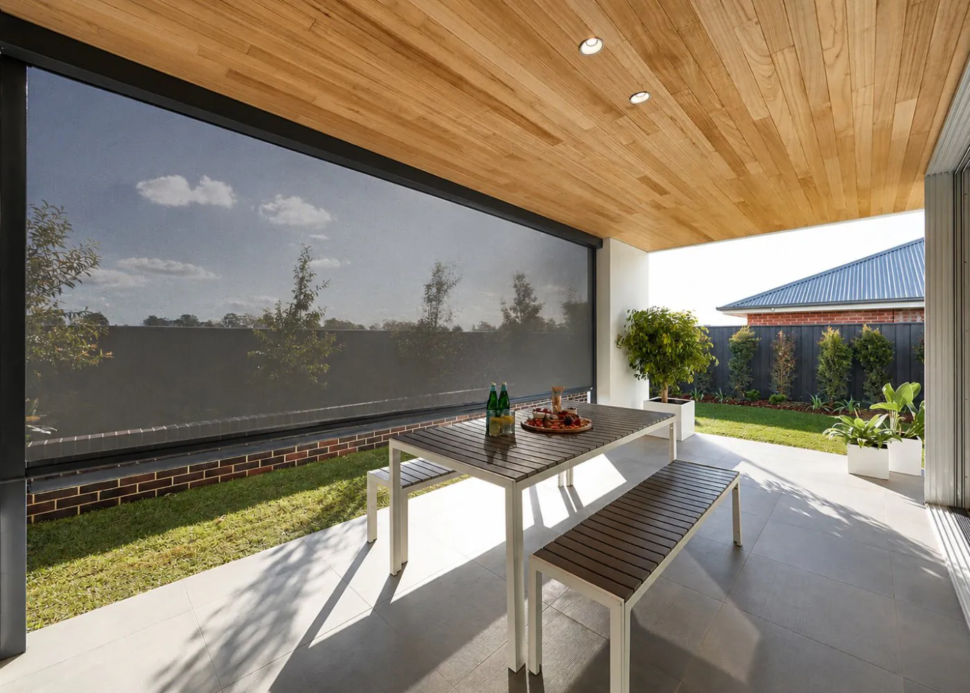 Looking out from a covered patio through a lowered grey mesh screen, with the lawn and trees still visible