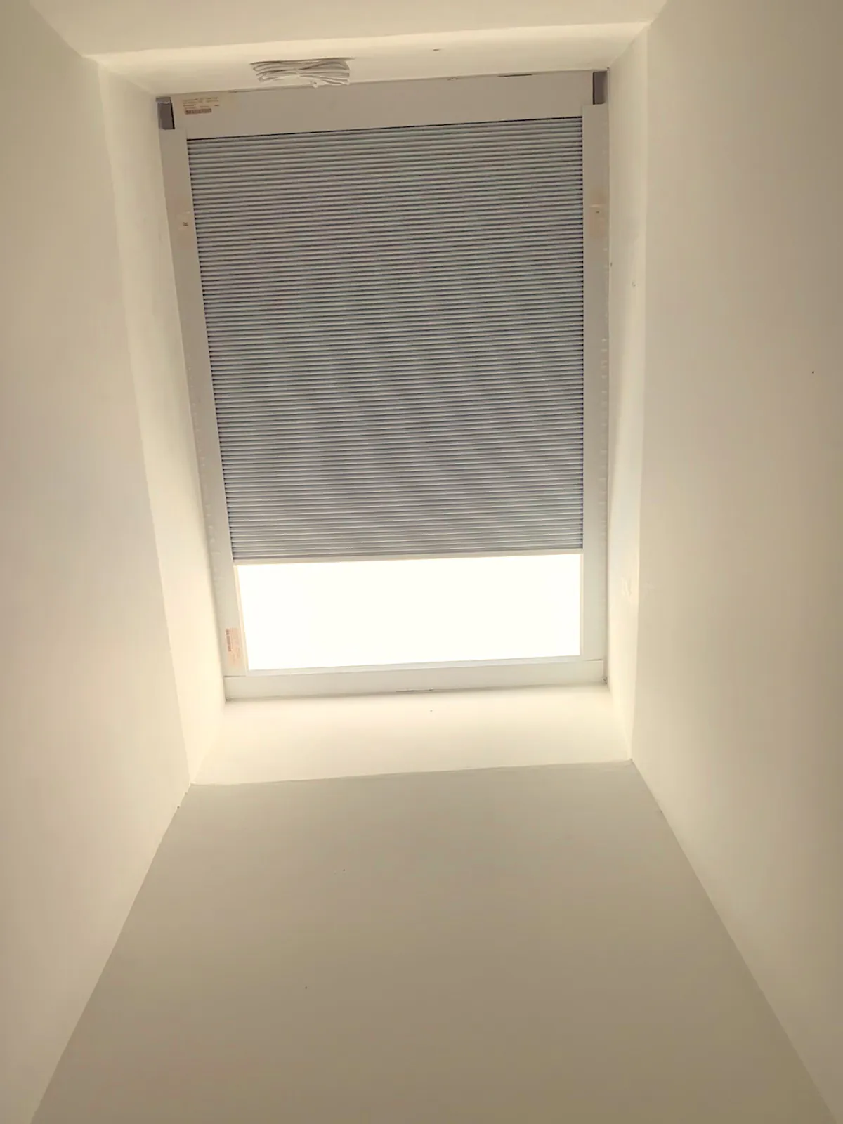 The same skylight with the cellular shade fully drawn across, only a thin line of daylight at the edge