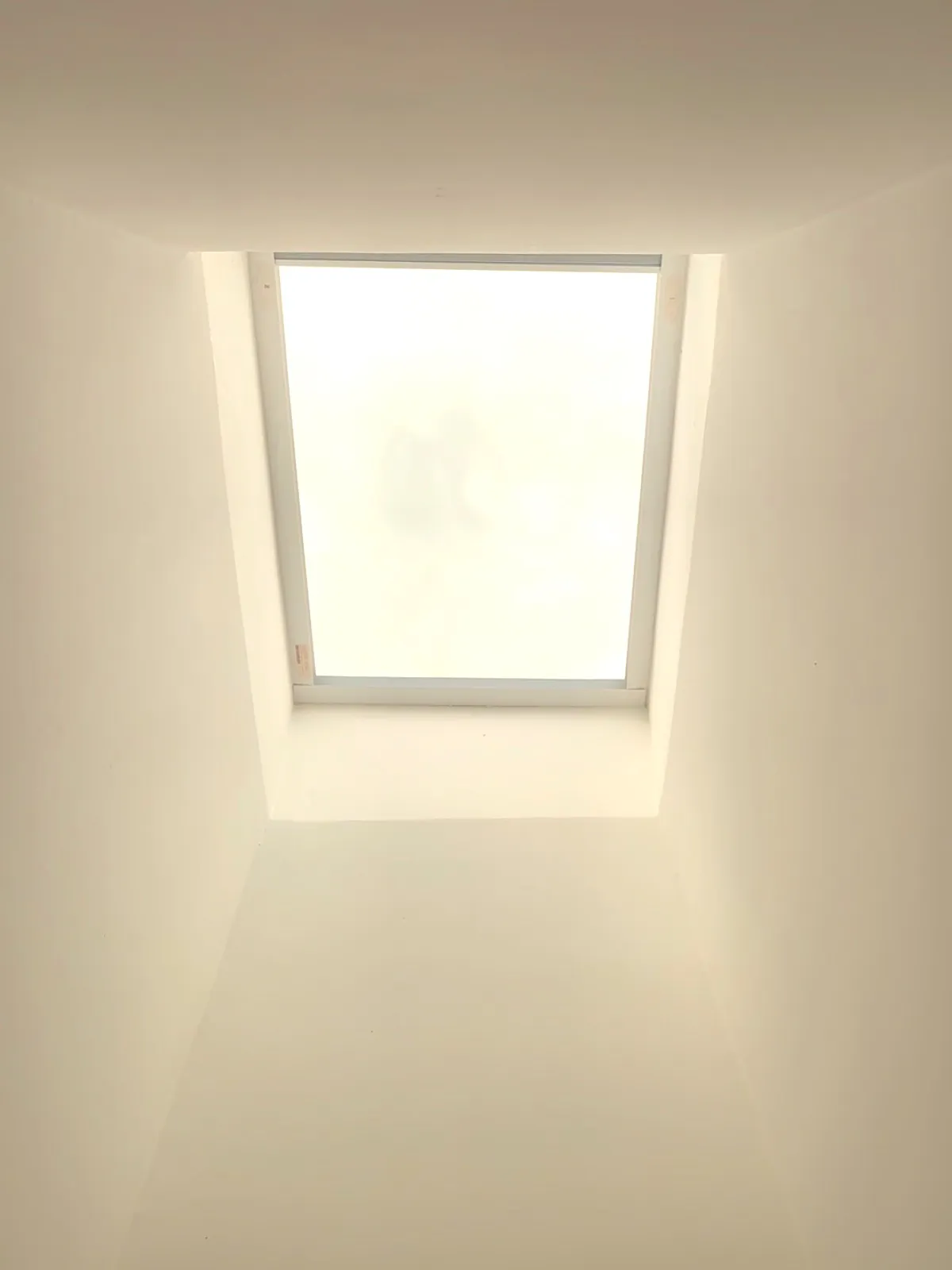 A skylight fully open with the cellular shade retracted into its head rail, bright sky above