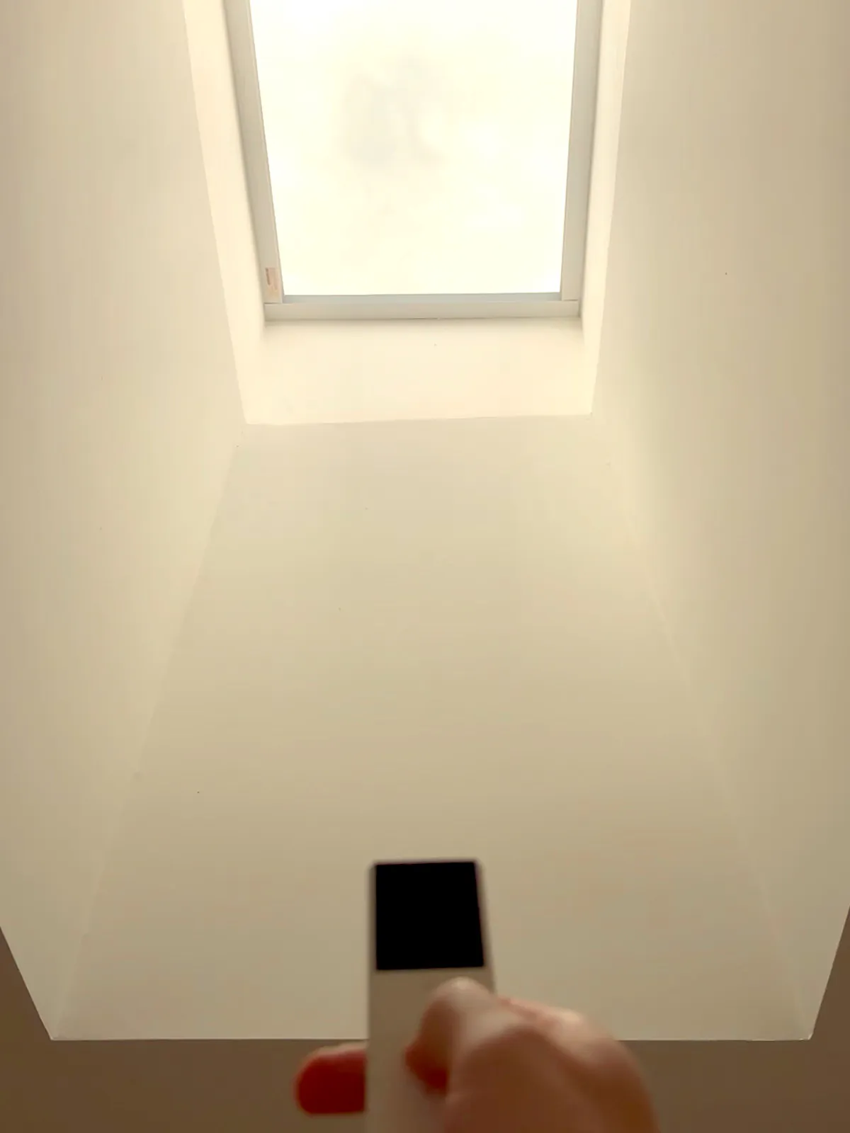 A hand holding the remote control below the skylight, shade retracted overhead